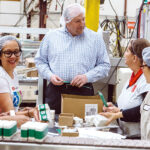 HELP WANTED: Bradford Soap Works Inc. in West Warwick is one of numerous Rhode Island companies hiring even though the economy has hit the skids during the corona­virus pandemic. In this 2018 file photo, CEO and President Stuart Benton works on the packing floor with Bradford employees. / PBN FILE PHOTO/RUPERT WHITELEY