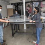 NEW DESIGN: The staff at Loft LLC, an industrial design company, has recently pivoted its work to designing and building contactless COVID-19 testing trailers for use by the National Guard. From left, Scott Noh, product design; Jeanette Numbers, co-founder; Nari Shin, designer/textile specialist. In the background is David Baker, director of engineering. / PBN PHOTO/MICHAEL SALERNO