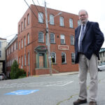 NEW LIFE: Joseph Garlick, executive director of NeighborWorks Blackstone River Valley, outside one of the downtown Woonsocket mill buildings that the organization is converting into live-work space for artists and businesses. / PBN PHOTO/ELIZABETH GRAHAM