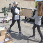 HANDOFF: Inspiring Minds, a nonprofit that works to mentor and tutor students in the Providence area, is delivering books to students during the COVID-19 pandemic. Executive Director Melissa Emidy, left, hands a box of books to Lisa Pierce. / PBN PHOTO/MICHAEL SALERNO