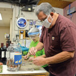 ROLLING WITH THE PUNCHES: Richard “Rippy” Serra, owner of Rippy’s Liquor and Marketplace in Charlestown, and office manager Donna McAdams roll coins brought in by customers. In an effort to combat the national coin shortage, Serra offers free coin rolling to customers to exchange their coins for dollar bills. / PBN PHOTO/ELIZABETH GRAHAM