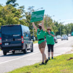 SIGN OF THE TIMES: Members of Keep Metacomet Green! attempt to drum up support recently outside the entrance to the Metacomet Golf Club, the site of a proposed residential and commercial development. / PBN PHOTO/MICHAEL SALERNO