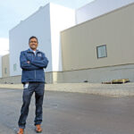 R.I. EXPANSION: Rohan Persaud, plant manager and executive director at Amgen Rhode Island, stands outside the company’s new next-generation biomanufacturing plant in West Greenwich. He is overseeing the startup and licensing of the facility.  / PBN PHOTO/ELIZABETH GRAHAM