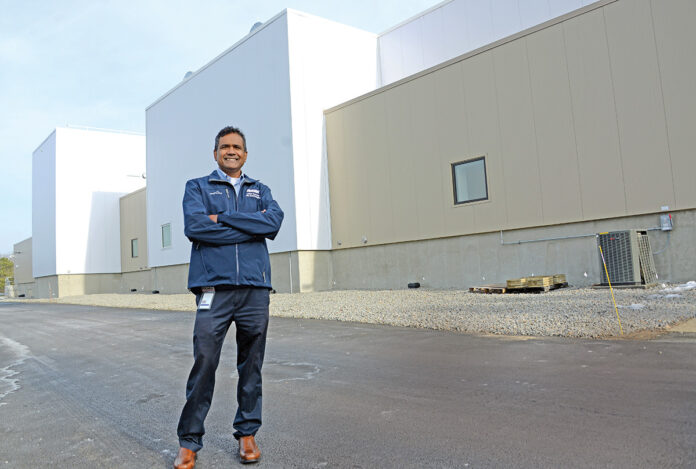 R.I. EXPANSION: Rohan Persaud, plant manager and executive director at Amgen Rhode Island, stands outside the company’s new next-generation biomanufacturing plant in West Greenwich. He is overseeing the startup and licensing of the facility.  / PBN PHOTO/ELIZABETH GRAHAM