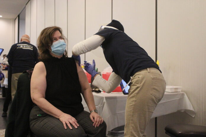 ELIZABETH MCKENNA, left, of Pawtucket receives her COVID-19 vaccination Thursday from Rhode Island Disaster Medical Assistance volunteer Kristen Poshkus at Kirkbrae Country Club in Lincoln. / PBN PHOTO/JAMES BESSETTE
