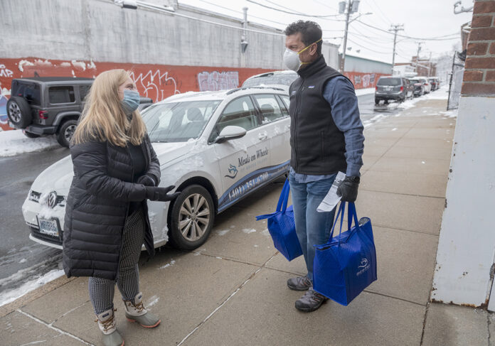 LOADING UP: Meg Grady, executive director for Meals on Wheels of Rhode Island, and volunteer Ted Fischer, CEO of Ageless Innovation, help load food into vehicles for some deliveries. Grady said the organization’s home-delivery program saw a 7% increase in seniors served and a 9% increase in meals served in 2020 compared with 2019. / PBN PHOTO/MICHAEL SALERNO