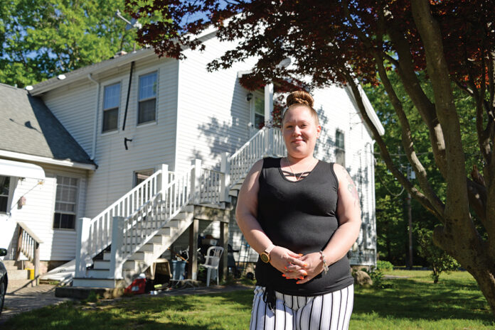 DOUBLE DUTY: Virginia Burdick, a certified nursing assistant and mother of two, stands in front of her two-bedroom apartment in South Kingstown. Burdick, who works two jobs to be able to afford the rent for the apartment, was recently approved by the South County Habitat for Humanity for one of its homes in Exeter, which she hopes to move into by the end of the year. / PBN PHOTO/ELIZABETH GRAHAM