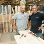 GROWING STAFF: Scott J. Pacheco, left, owner and president of Scott James Furniture & Design in Tiverton, with his father, Rob Pacheco, head bed builder. Although the company shut down for two months at the start of the pandemic in March 2020, it has done well since then, Scott Pacheco said, especially “doing a lot more work in the wealthier coastal neighborhoods for people leaving New York,” which has resulted in more full-time employees now than before COVID-19 hit. / PBN PHOTO/DAVE HANSEN