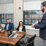 STEADY GROWTH: Cole DeSanty, right, director of client development for The Hire LLC, speaks with his colleagues, from left, CEO Tyler Wentworth; Bryan Soderberg, manager of candidate success; and Chief Operating Officer Erin Pavane. The Providence job placement firm has seen steady revenue growth since offering unlimited PTO from its inception in 2017. / PBN PHOTO/MICHAEL SALERNO
