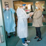 TAKING NO CHANCES: In November 2020, Elizabeth “Libby” Sarro, right, administrator at Bethany Home of Rhode Island, helps office manager Linda Wilson, center, and David Bragga, director of therapy, don protective equipment at the entrance of the Providence nursing home. / PBN FILE PHOTO/MICHAEL SALERNO