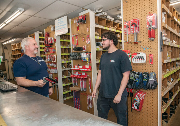 NEXT GEN: M&G Plumbing Supply Co. owner Richard Correia, left, speaks with stock clerk Alex Knowles. Correia is of Portuguese descent but sees no need to participate in the state Minority Business Enterprise program. His father, John, emigrated from the Azores and started in the business in the 1960s. / PBN PHOTO/MICHAEL SALERNO