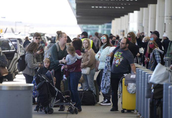 TRAVELERS LINE UP at the Southwest Airlines curbside check-in area at Denver International on Sunday. Airlines canceled hundreds of flights Sunday, citing staffing problems tied to COVID-19 to extend the nation's travel problems beyond Christmas. AP PHOTO/DAVID ZALUBOWSKI