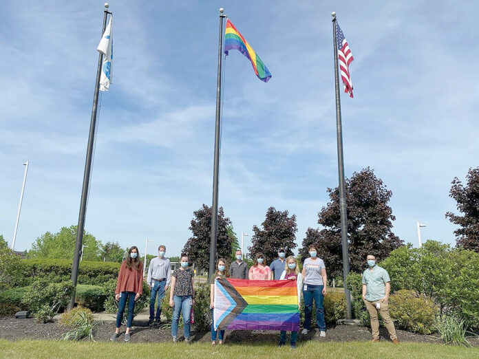 PROUD DISPLAY: Amgen Inc. employees hold the progress pride flag, a variant of the pride flag, or the rainbow flag, a symbol of lesbian, gay, bisexual, transgender and queer pride, which flies overhead on the center flag pole at the company’s West Greenwich campus.  COURTESY AMGEN INC.
