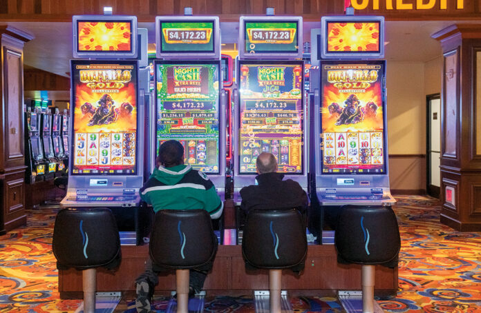 REVENUE STREAM: Two people try their luck at video slot machines at Bally’s Twin River Lincoln Casino. Revenue generated through slot machines and table games at Rhode Island’s two casinos, in combination with lottery tickets and drawings, is one of the biggest sources of funding for the state’s $13 billion budget. / PBN PHOTO/ MICHAEL SALERNO