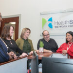 ­COORDINATING COVERAGE: HealthSource RI Director Lindsay Lang, third from left, meets with staff members, from left, Contessa Brown, senior analyst; Leslie Racine Vazquez, operations manager; and Steve Micke and Katherine Rivera in customer service. / PBN PHOTO/MICHAEL SALERNO