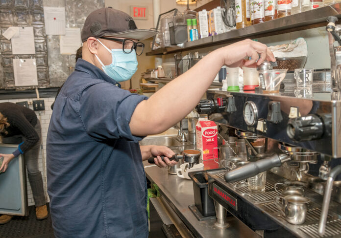 BOLD MOVE: Christian Rakotoarisoa makes a latte at White Electric Coffee in Providence. Rakotoarisoa is one of nine worker-owners at White Electric, which became the first unionized worker-owned cooperative cafe in Rhode Island last year. / PBN PHOTO/MICHAEL SALERNO