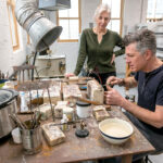 MALLEABLE METALLERS: Sandi Bonazoli and Jim Dowd are the co-owners of Beehive Handmade, a long-standing metal­work business that recently opened a store and studio space in Warren. Dowd crafts a copper rack for measuring spoons while Bonazoli looks on. / PBN PHOTO/MICHAEL SALERNO