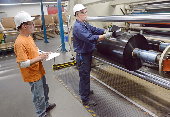 HIGH ROLLER: Greg Viera, left, a machine operator, and Frank Costa, ­senior machine operator, work on the manufacturing floor at plastics maker Trico Specialty Films Inc. in North Kingstown.  PBN PHOTO/ELIZABETH GRAHAM