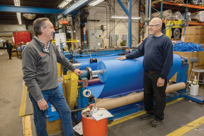RESILIENT WORKFORCE: Daniel Dwight, left, CEO and president of Cooley Group in Pawtucket, speaks with machine operator ­Henry DaSilva. Dwight says his core motivation is to inspire his team to maintain optimism in the face of an ever-changing environment. PBN PHOTO/TRACY JENKINS