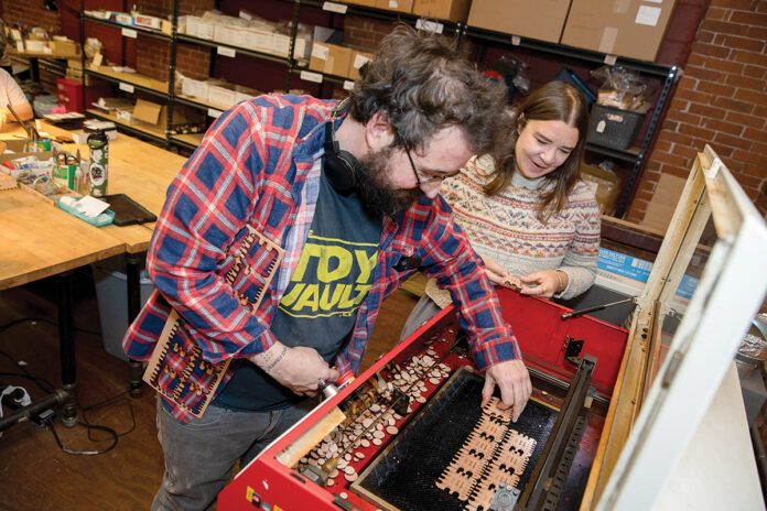 WHIMSICAL PRODUCTS: Katy Westscott, CEO of Katrinkles Inc. in Providence, which makes buttons and tools for crafters, goes over some of the company’s products with production technician Brandon Amorin. PBN PHOTO/TRACY JENKINS