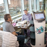 ROLLING OUT: Jacky’s Waterplace Sushi Bar robot server “Bella” waits on a table with Ignacio Davila, left, and Galen Tate. PBN PHOTO/­MICHAEL SALERNO