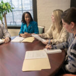 TABLE TALK: Anika Kimble-Huntley, second from left, chief marketing officer at R.I. Commerce Corp., confers with her staff at the R.I. Commerce headquarters in Providence. The staff includes, from left, Mark Brodeur, director of international and domestic group sales; Lindsay Russell, deputy director of communications and stakeholder engagement; and Robin Erickson, domestic tourism and marketing operations director. PBN PHOTO/MICHAEL SALERNO