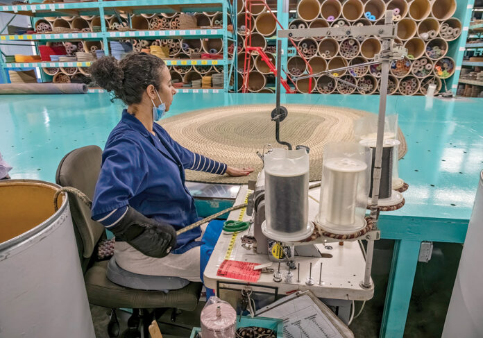 TIGHTKNIT OPERATION: Employee Maria Monteiro works on a rug at Rhody Rug Inc.’s manufacturing facility in Lincoln. The company produces 1,500 braided rugs per week and supplies hundreds of rug dealers nationwide, says President Scott Weldon. PBN PHOTO/MICHAEL SALERNO